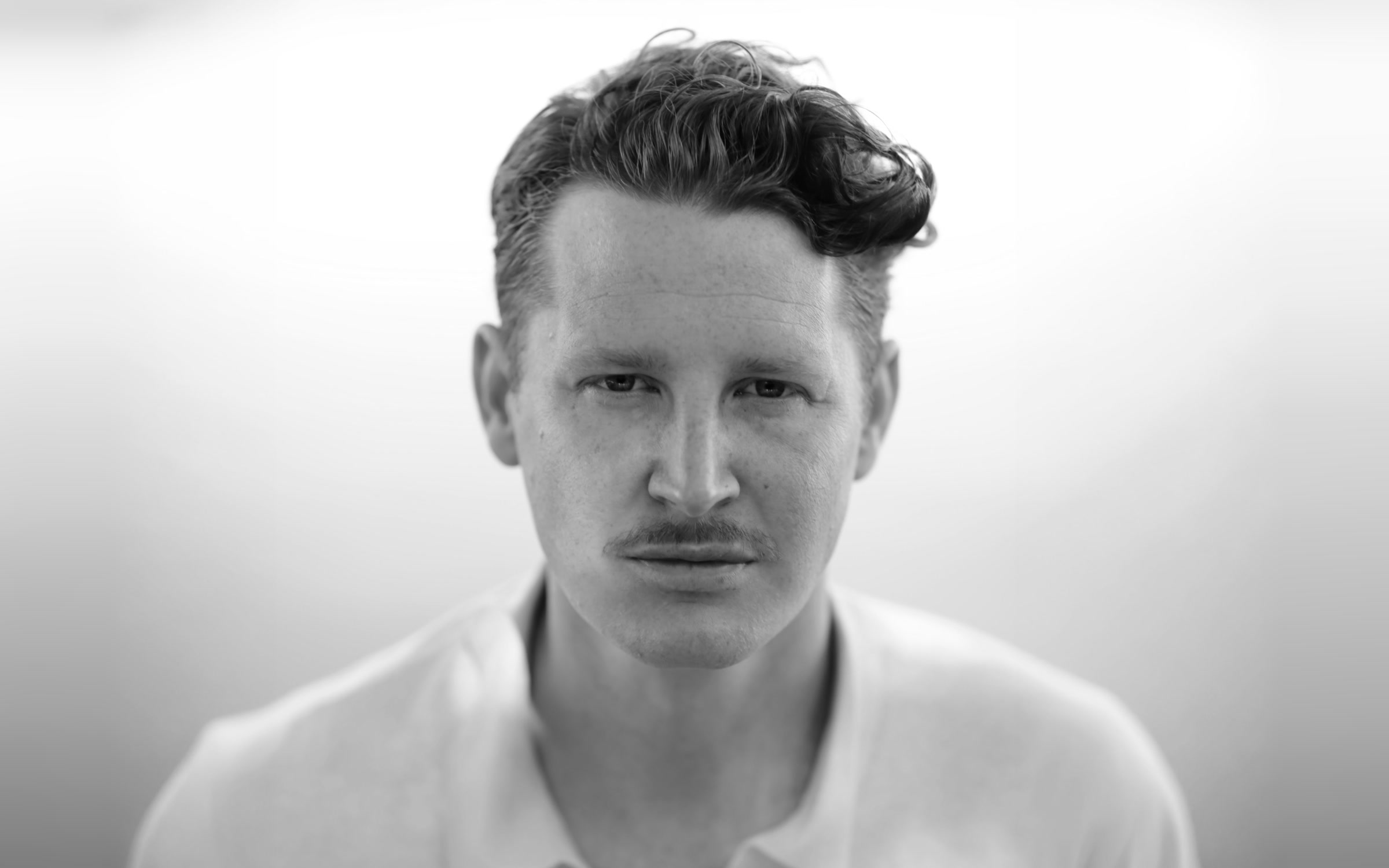 Benjamin Noble, a black and white portrait in a pale open-collar shirt